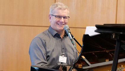 Pastor und Klinikseelsorger Roger Bahr sitzt am Klavier mit einem Mikrofon und trägt ein Stück vor bei der Weihnachtsfeier 2025 von Amalie Sieveking Krankenhaus, Residenz am Wiesenkamp, Feierabendhaus Volksdorf und Albertinen Kindertagesstätte Volksdorf auf dem Gesundheitscampus Volksdorf in Hamburg