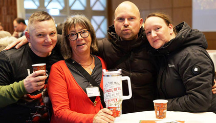 Vier Mitarbeitende stehen an einem Tisch, halten Getränkebecher und Trinkgefäße hoch und blicken fröhlich in die Kamera bei der Weihnachtsfeier 2025 von Amalie Sieveking Krankenhaus, Residenz am Wiesenkamp, Feierabendhaus Volksdorf und Albertinen Kindertagesstätte Volksdorf auf dem Gesundheitscampus Volksdorf in Hamburg