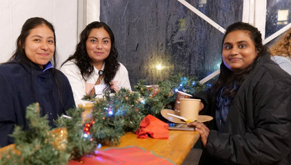 Drei Frauen sitzen an einer mit Zweigen und Weihnachtsdeko geschmückten Sitzgarnitur im Festzelt und blicken in die Kamera bei der Weihnachtsfeier 2025 von Amalie Sieveking Krankenhaus, Residenz am Wiesenkamp, Feierabendhaus Volksdorf und Albertinen Kindertagesstätte Volksdorf auf dem Gesundheitscampus Volksdorf in Hamburg