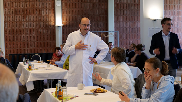 Prof. Dr. med. Ernst von Dobschütz, Chefarzt Zentrum für Endokrine Chirurgie und Ärztlicher Direktor, steht im Veranstaltungsraum und unterhält sich mit einer Kollegin bei der Fachveranstaltung 11. Amalie Tag der Hausärztinnen und Hausärzte im Evangelischen Amalie Sieveking Krankenhaus in Hamburg-Volksdorf.