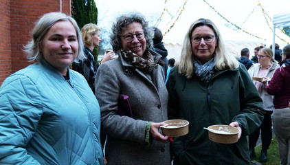 Drei Gäste blicken in die Kamera und halten in Schalen verpacktes Essen in der Hand bei der Weihnachtsfeier 2025 von Amalie Sieveking Krankenhaus, Residenz am Wiesenkamp, Feierabendhaus Volksdorf und Albertinen Kindertagesstätte Volksdorf auf dem Gesundheitscampus Volksdorf in Hamburg